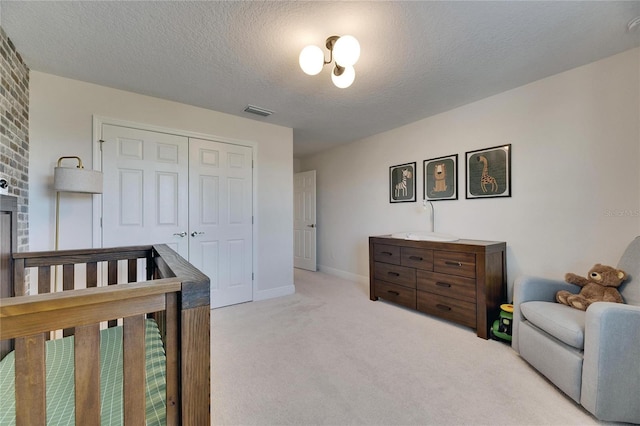 carpeted bedroom featuring a crib, a textured ceiling, and a closet