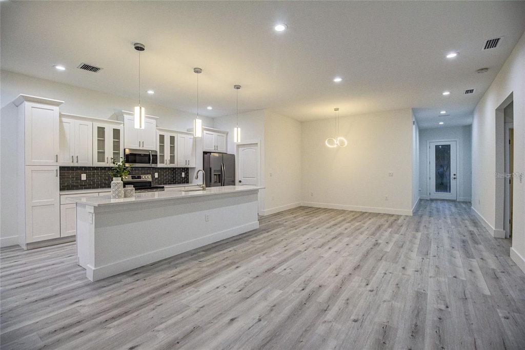 kitchen featuring appliances with stainless steel finishes, light wood-type flooring, decorative light fixtures, a center island with sink, and white cabinetry