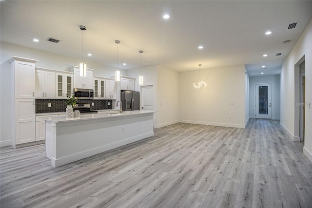 kitchen featuring appliances with stainless steel finishes, light wood-type flooring, decorative light fixtures, a center island with sink, and white cabinetry