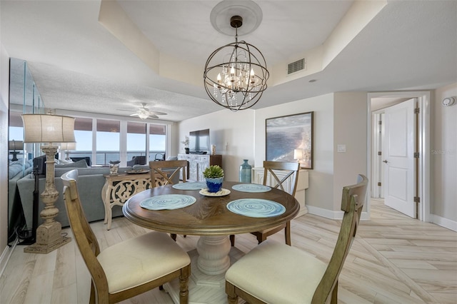 dining room featuring light wood-type flooring, ceiling fan with notable chandelier, and a tray ceiling