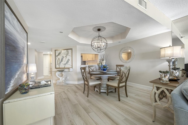 dining room featuring a raised ceiling, light wood-type flooring, and an inviting chandelier