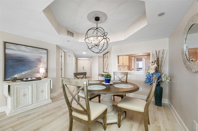 dining area with a raised ceiling, light hardwood / wood-style flooring, a textured ceiling, and an inviting chandelier