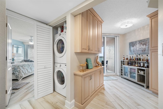 clothes washing area with a textured ceiling, ceiling fan, stacked washer / drying machine, and light wood-type flooring