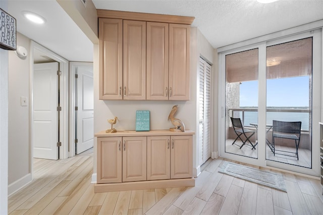 kitchen with light brown cabinetry, a water view, a textured ceiling, and light wood-type flooring