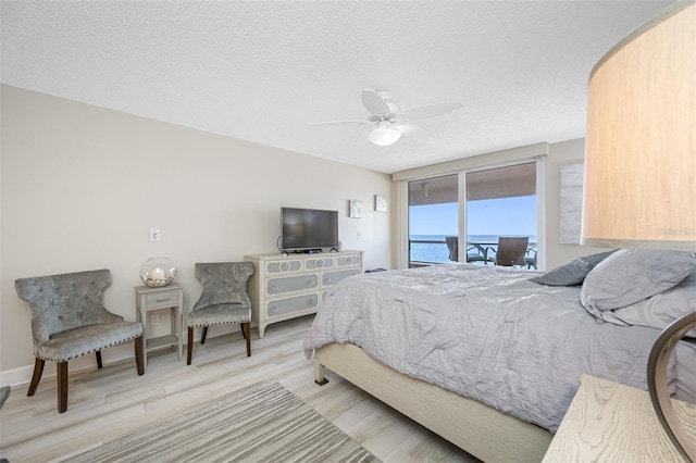 bedroom with ceiling fan, access to exterior, a textured ceiling, and light hardwood / wood-style flooring