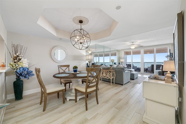 dining space featuring a raised ceiling, a water view, light hardwood / wood-style floors, and ceiling fan with notable chandelier