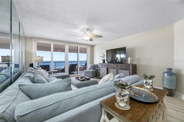 living room with ceiling fan, a textured ceiling, and light wood-type flooring