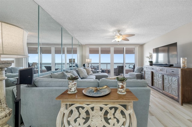 living room featuring a textured ceiling, light wood-type flooring, expansive windows, and ceiling fan