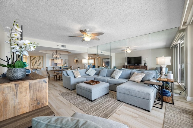 living room with a textured ceiling, ceiling fan with notable chandelier, and light wood-type flooring