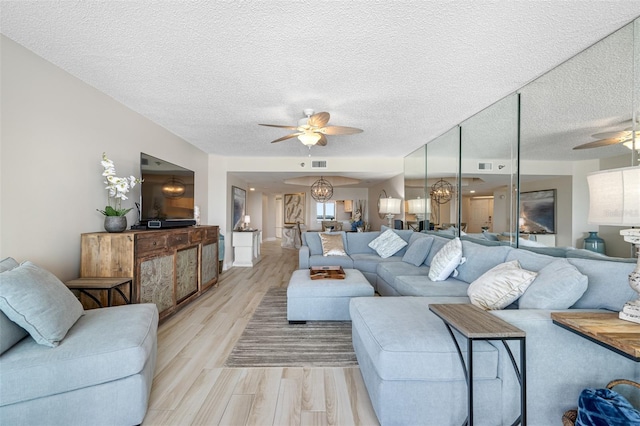 living room featuring ceiling fan, light hardwood / wood-style floors, and a textured ceiling