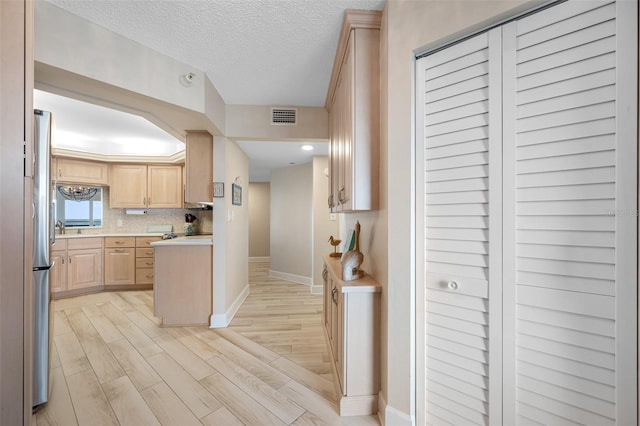 kitchen with backsplash, light hardwood / wood-style flooring, stainless steel fridge, a textured ceiling, and light brown cabinetry