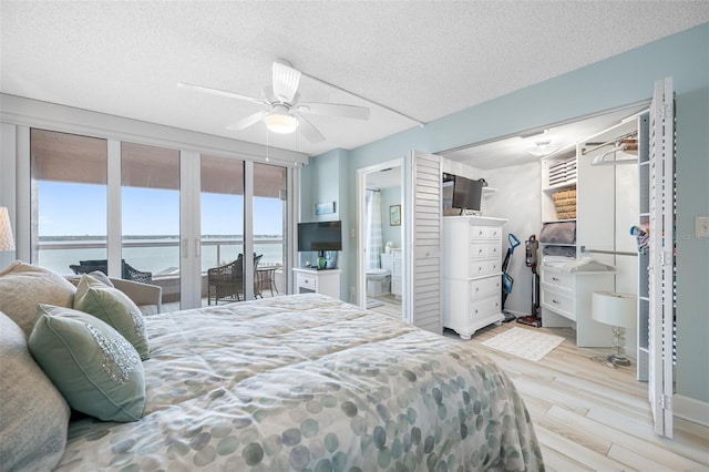 bedroom with access to exterior, a textured ceiling, ceiling fan, a water view, and multiple windows