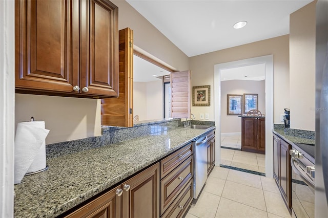 kitchen with stainless steel dishwasher, sink, light tile patterned floors, stone counters, and range