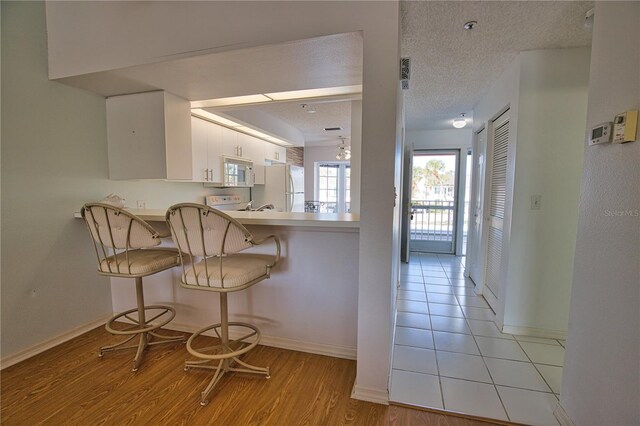 201 Silver Lake Dr Unit 204, Venice, FL 34292 - kitchen featuring a breakfast bar, white appliances, a peninsula, white cabinetry, and light wood-type flooring