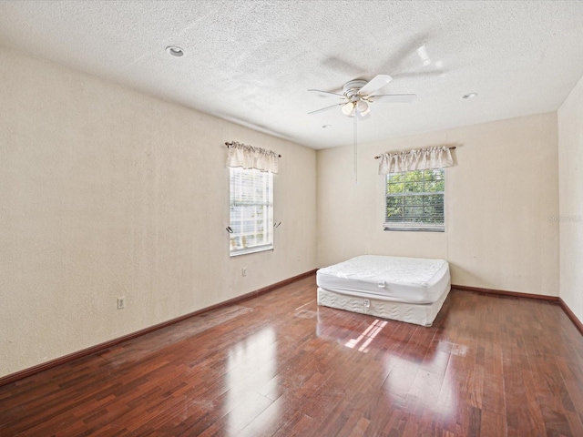 unfurnished bedroom featuring hardwood / wood-style flooring, ceiling fan, a textured ceiling, and multiple windows