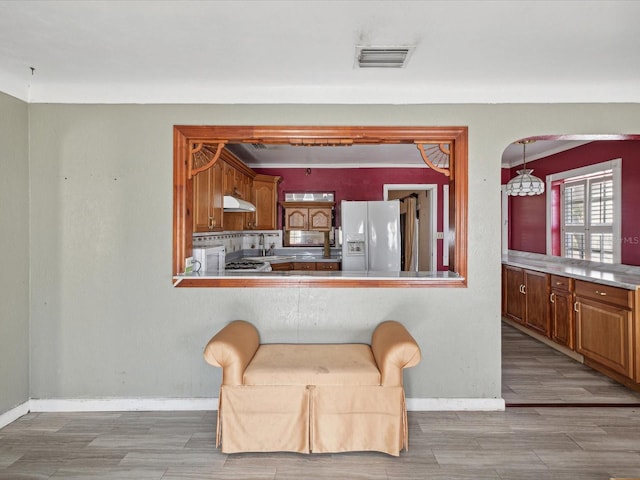 kitchen featuring a kitchen breakfast bar, light hardwood / wood-style flooring, decorative light fixtures, and white refrigerator with ice dispenser