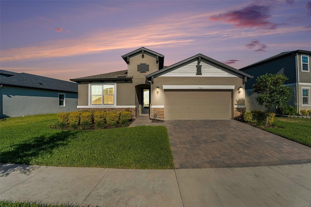 view of front of property with an attached garage, a yard, stone siding, decorative driveway, and stucco siding