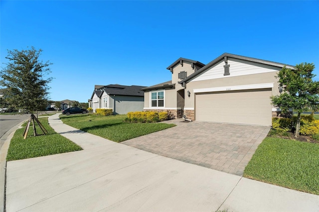 view of front of property featuring decorative driveway, stucco siding, an attached garage, a front yard, and stone siding