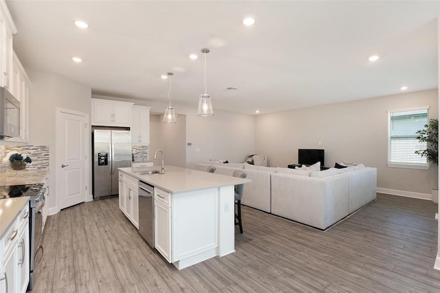 kitchen with appliances with stainless steel finishes, open floor plan, backsplash, light wood-style floors, and a sink