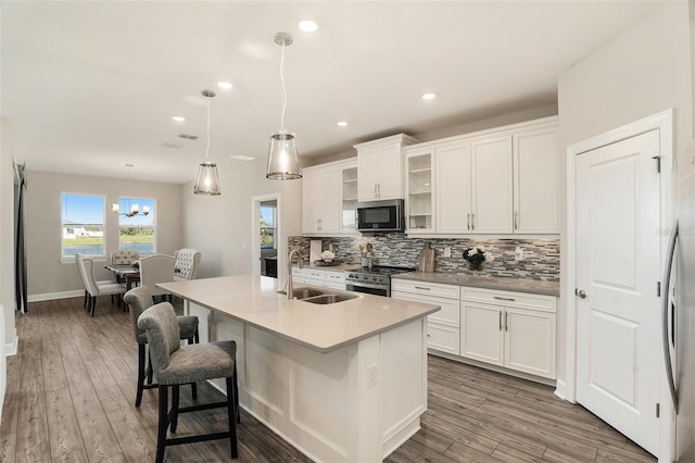 kitchen featuring stainless steel appliances, backsplash, white cabinetry, a sink, and wood finished floors