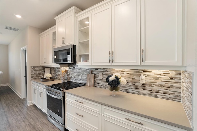 kitchen with stainless steel appliances, visible vents, light wood-style floors, white cabinetry, and tasteful backsplash