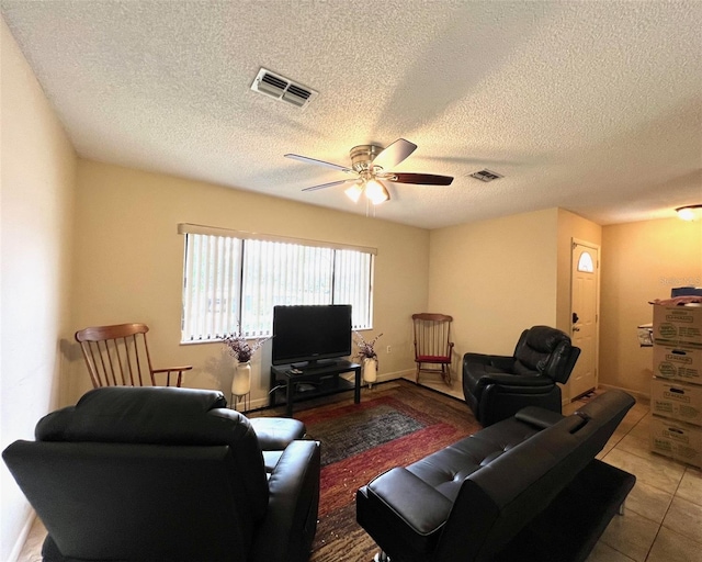 living room featuring tile patterned floors, visible vents, a textured ceiling, and ceiling fan