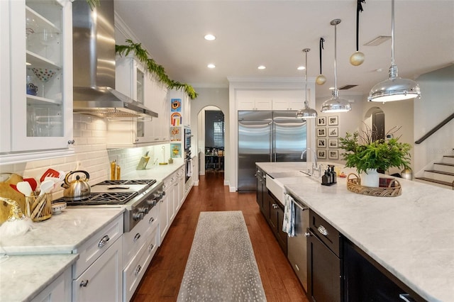 kitchen with light stone counters, decorative light fixtures, appliances with stainless steel finishes, range hood, and white cabinets