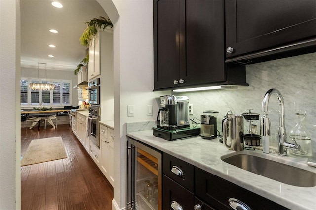 kitchen featuring dark hardwood / wood-style floors, decorative light fixtures, sink, wine cooler, and light stone counters