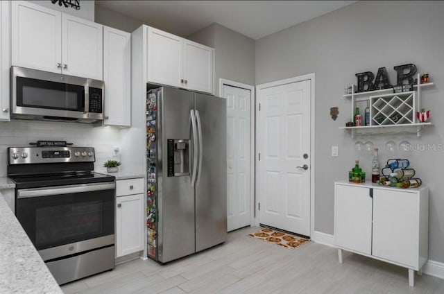 kitchen featuring white cabinets, appliances with stainless steel finishes, backsplash, and light wood-type flooring