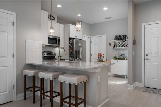 kitchen with kitchen peninsula, appliances with stainless steel finishes, pendant lighting, white cabinets, and a breakfast bar area