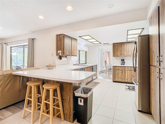 kitchen with sink, kitchen peninsula, a breakfast bar area, light tile patterned flooring, and appliances with stainless steel finishes