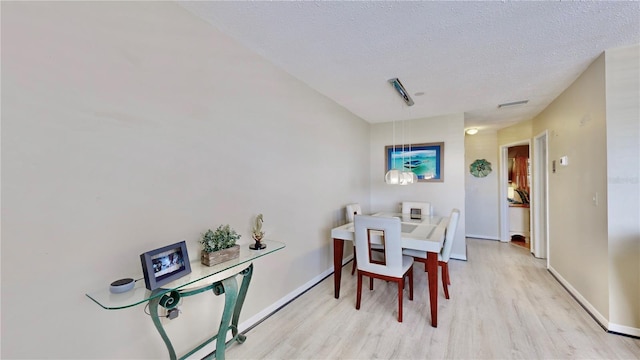 dining room featuring light wood-type flooring and a textured ceiling