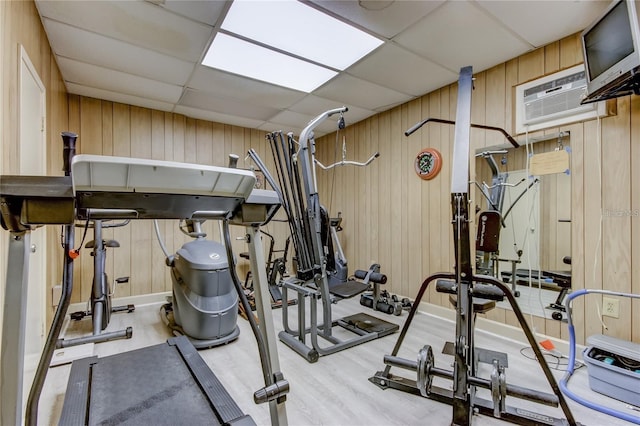 exercise room featuring a wall mounted air conditioner, a drop ceiling, and wooden walls