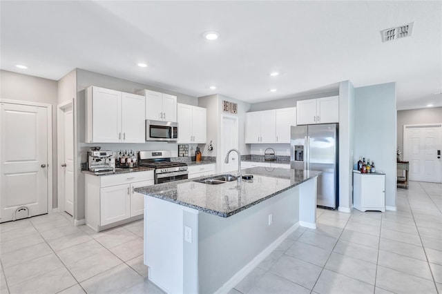 kitchen featuring sink, stainless steel appliances, dark stone countertops, a kitchen island with sink, and white cabinets