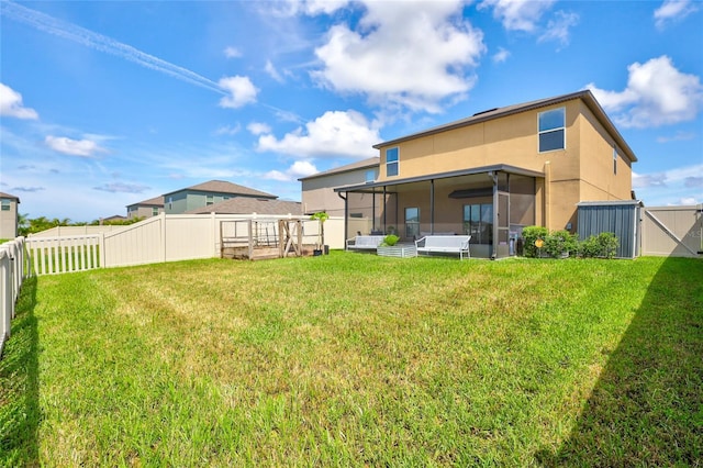 rear view of house with a lawn, a sunroom, a fenced backyard, a gate, and stucco siding