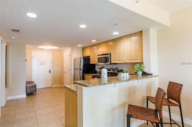 kitchen with kitchen peninsula, light stone countertops, light tile patterned floors, and appliances with stainless steel finishes