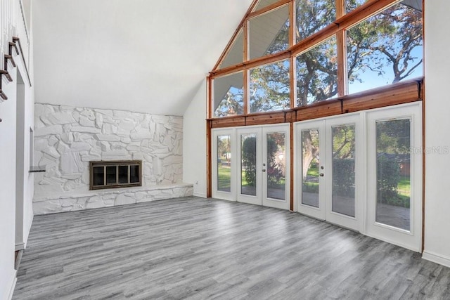 unfurnished living room featuring hardwood / wood-style floors, a stone fireplace, high vaulted ceiling, and french doors