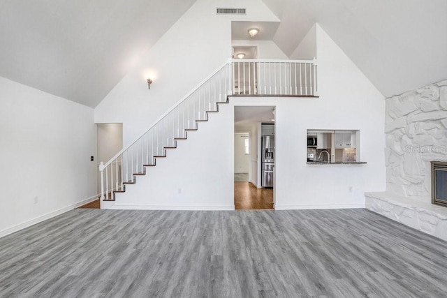 unfurnished living room featuring hardwood / wood-style floors, a towering ceiling, and a stone fireplace