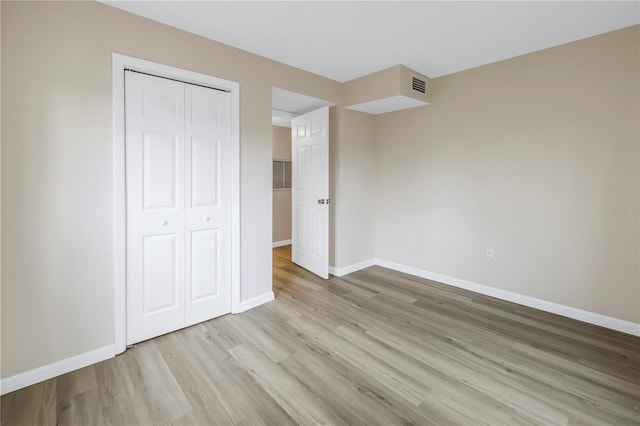 unfurnished bedroom featuring light wood-style flooring, a closet, visible vents, and baseboards