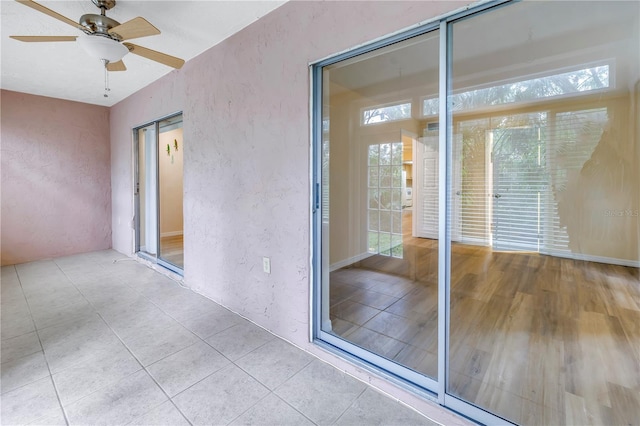 interior space with a ceiling fan, a textured wall, and light tile patterned floors