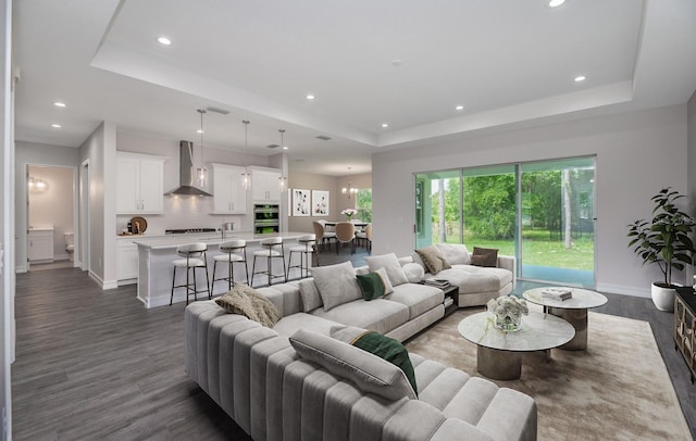 living room featuring dark wood-type flooring, a raised ceiling, and a notable chandelier