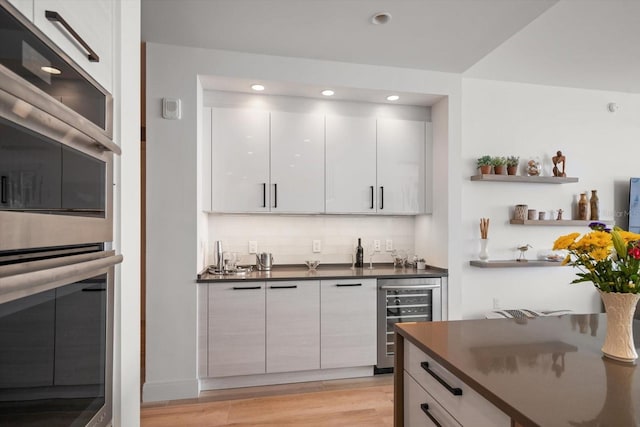 bar featuring decorative backsplash, double oven, beverage cooler, light hardwood / wood-style flooring, and white cabinets