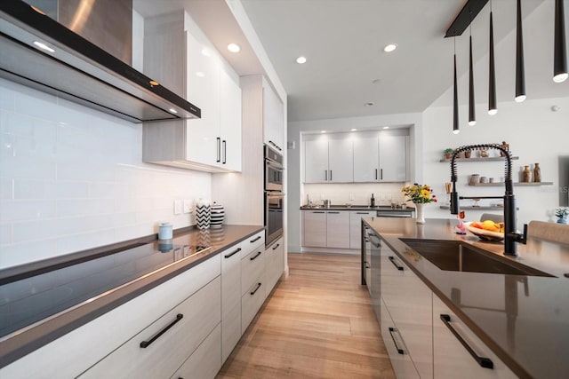 kitchen featuring white cabinets, wall chimney range hood, sink, light wood-type flooring, and stovetop