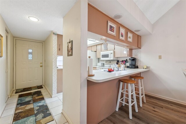 kitchen with white appliances, backsplash, light tile patterned floors, a textured ceiling, and kitchen peninsula