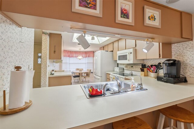 kitchen with a skylight, backsplash, kitchen peninsula, white appliances, and a breakfast bar area