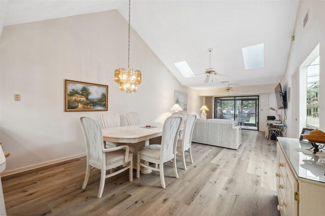 dining space featuring ceiling fan with notable chandelier, a skylight, light hardwood / wood-style flooring, and high vaulted ceiling