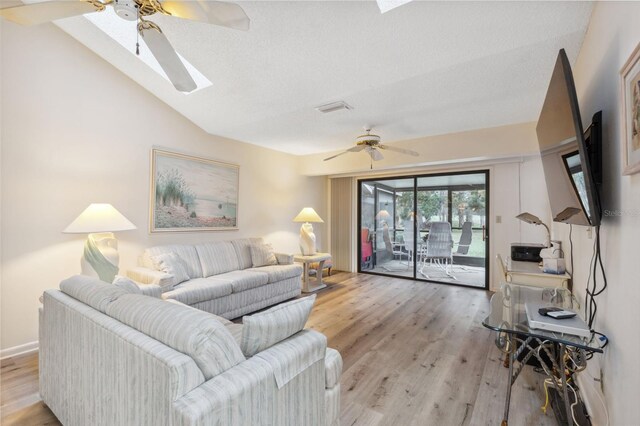 living room featuring ceiling fan, light hardwood / wood-style flooring, a textured ceiling, and vaulted ceiling with skylight