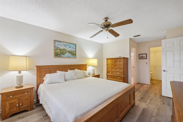 bedroom featuring a walk in closet, ceiling fan, a textured ceiling, light hardwood / wood-style floors, and a closet