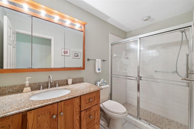 bathroom featuring tile patterned flooring, vanity, toilet, and a shower with shower door