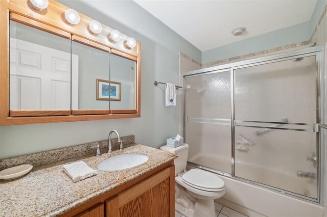 full bathroom featuring tile patterned floors, vanity, toilet, and bath / shower combo with glass door